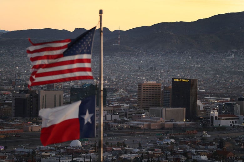 U.S. and state of Texas flags fly in the foreground as the cities of El Paso and Juarez stretch into the distance backdropped by mountains.